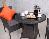 Brown rattan bistro table with glass top, coffee set, and wicker chair with orange cushion