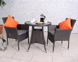 Rattan outdoor bistro set with round table, two chairs, grey cushions, and orange pillows