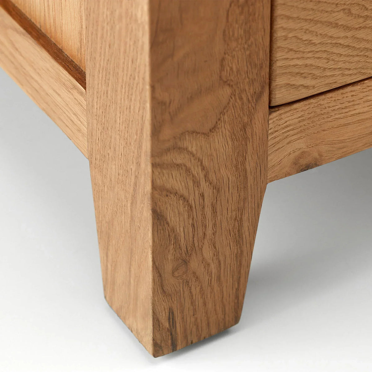 Oak bedside table leg and drawer corner detail on light background
