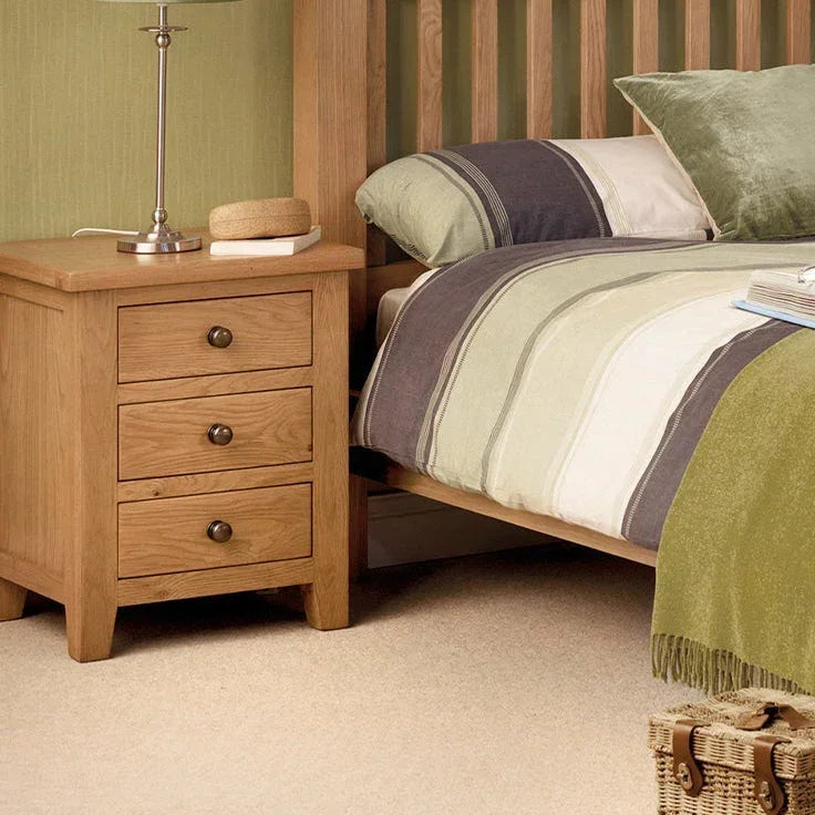 Oak 3 drawer bedside table beside slatted bed with striped bedding and lamp