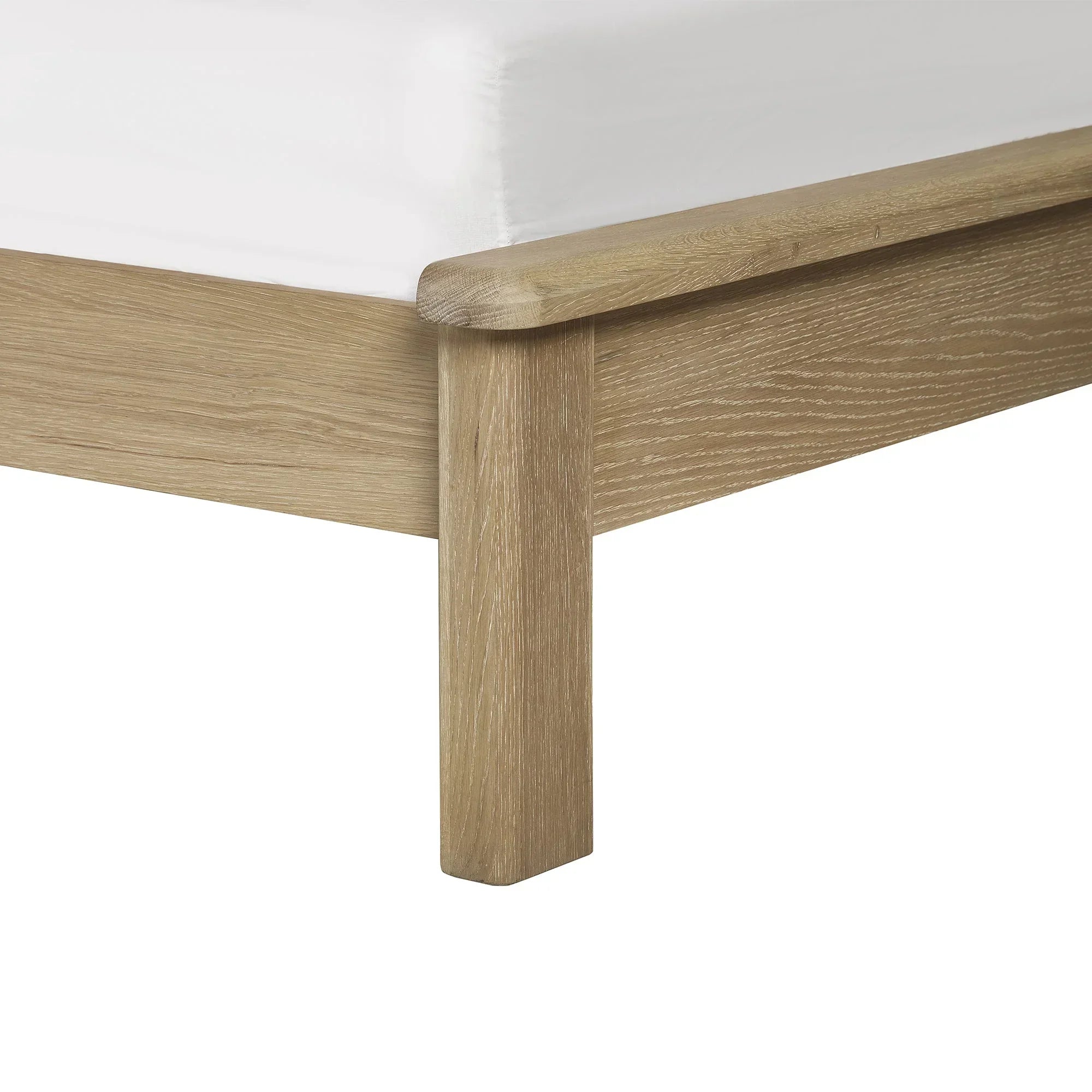 Closeup of limed oak bed frame leg with wood grain detail and white mattress