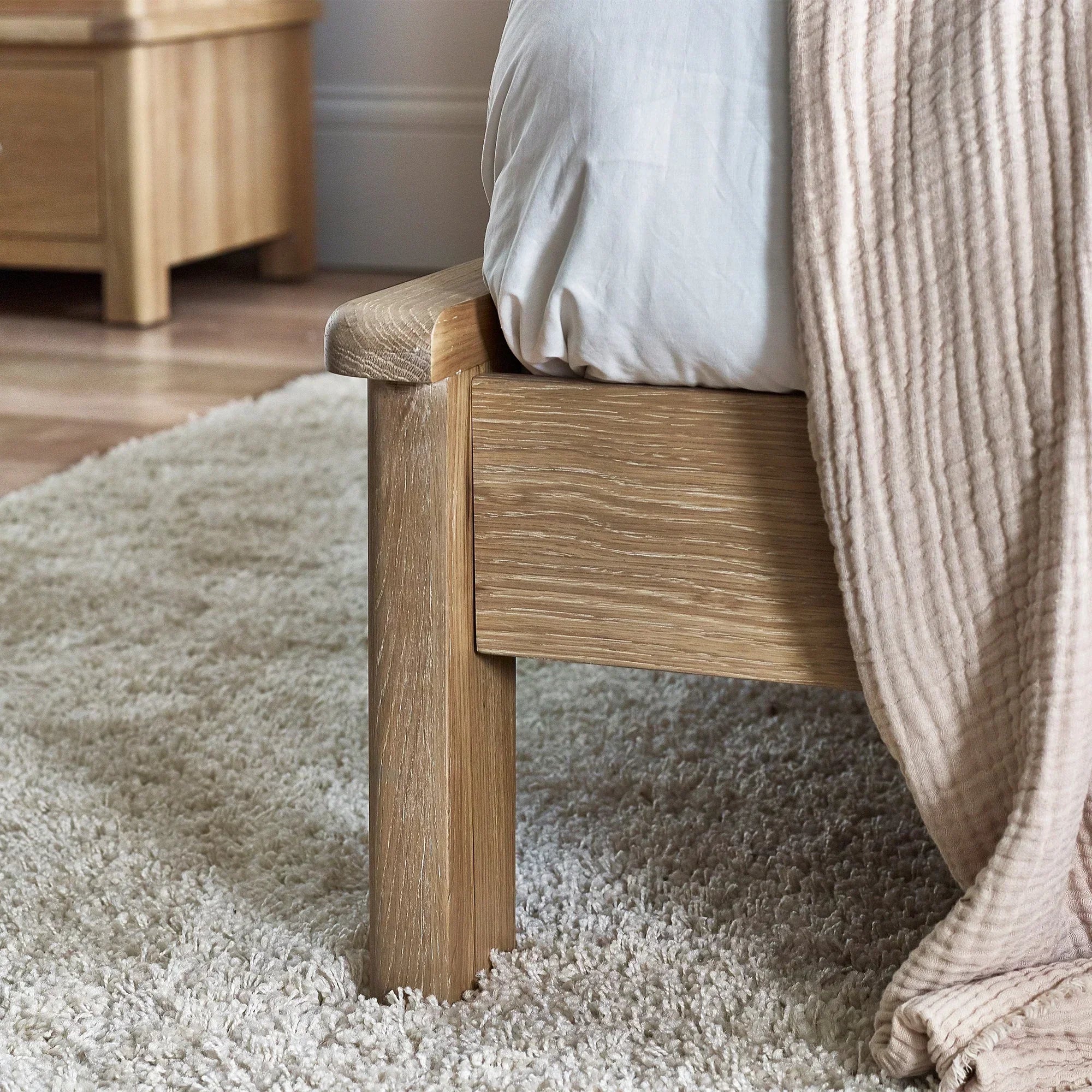 Close-up of limed oak bed frame with textured wood grain on cream carpet