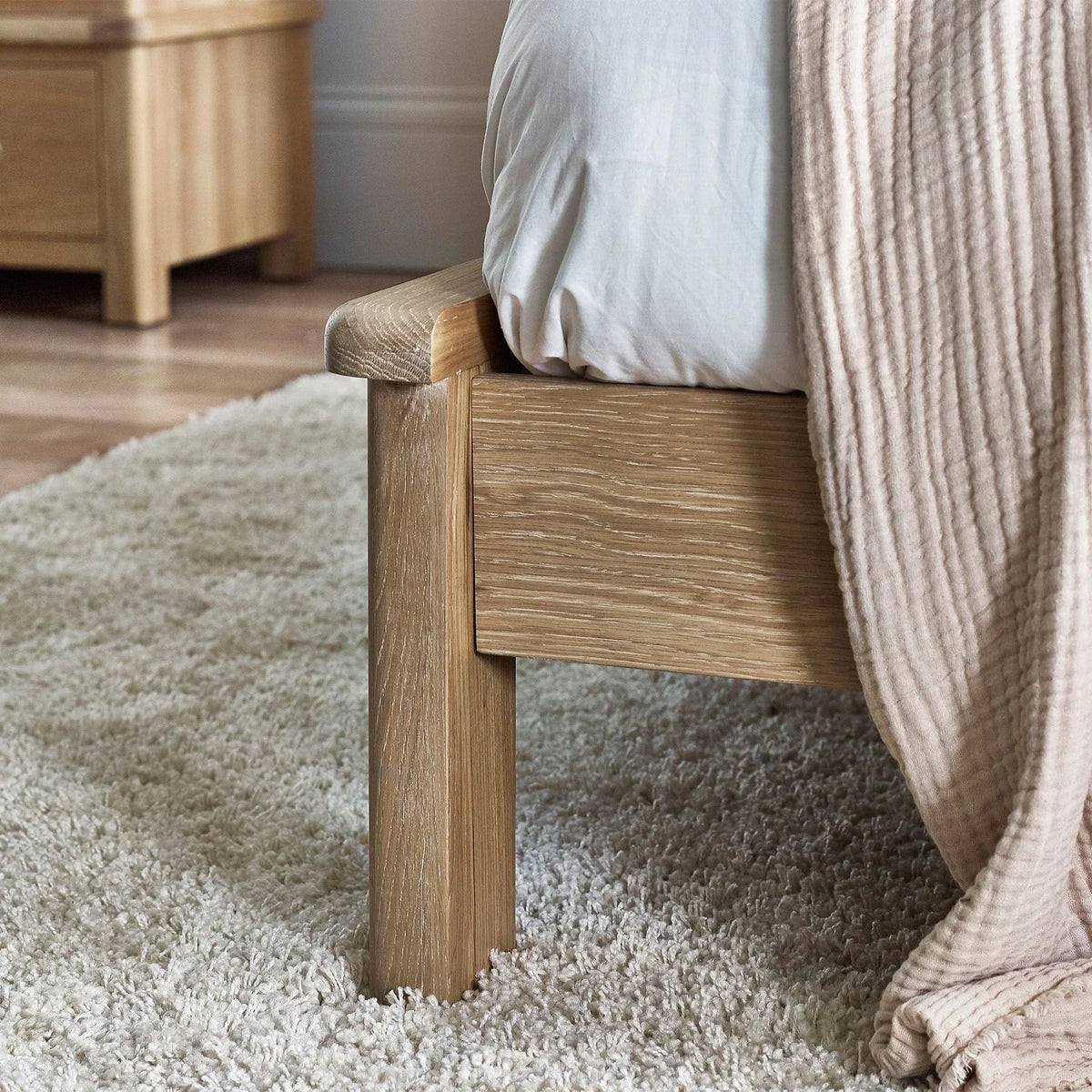 Close-up of limed oak bed frame with textured wood grain on cream carpet