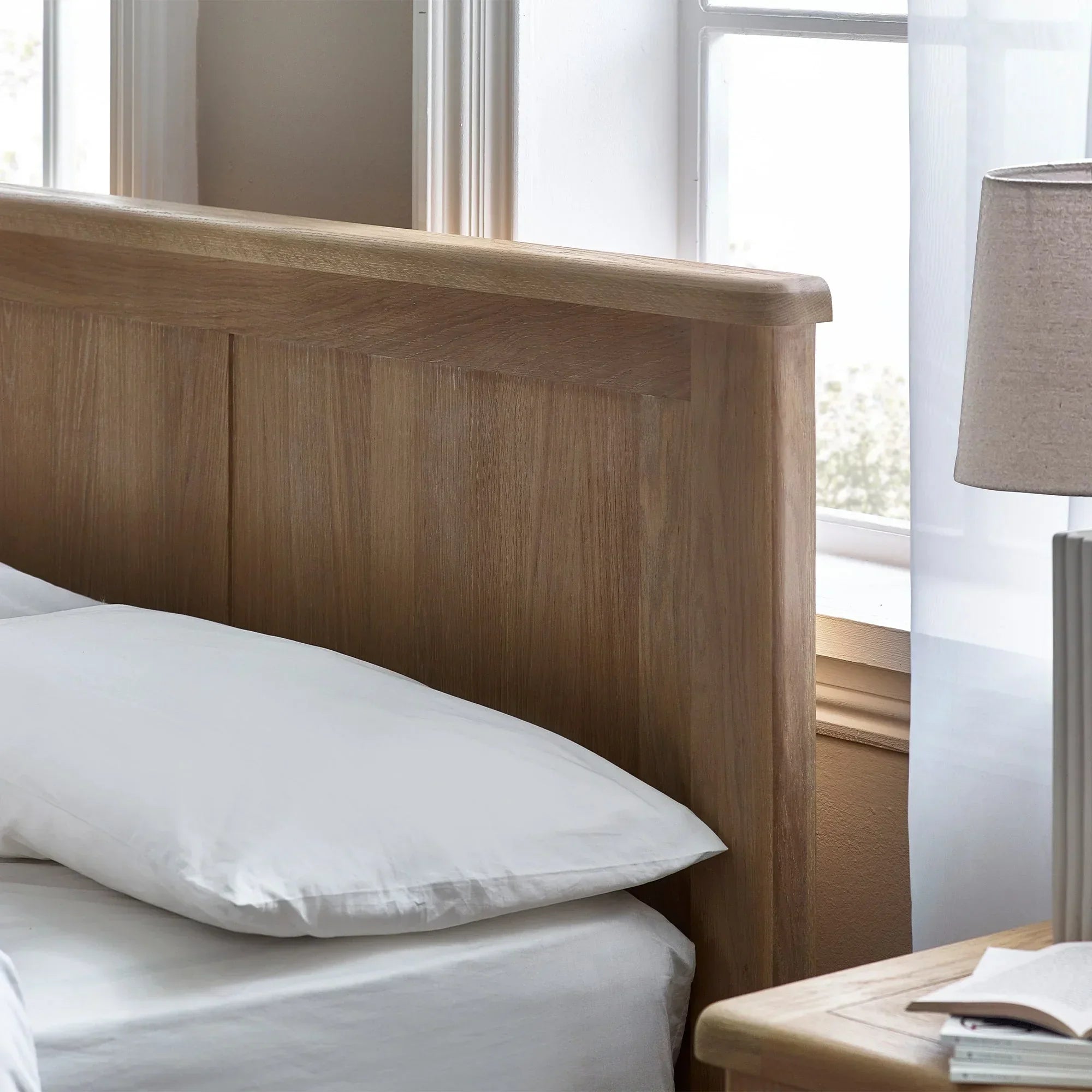 Close-up of Memphis limed oak bed frame headboard with white bedding by window