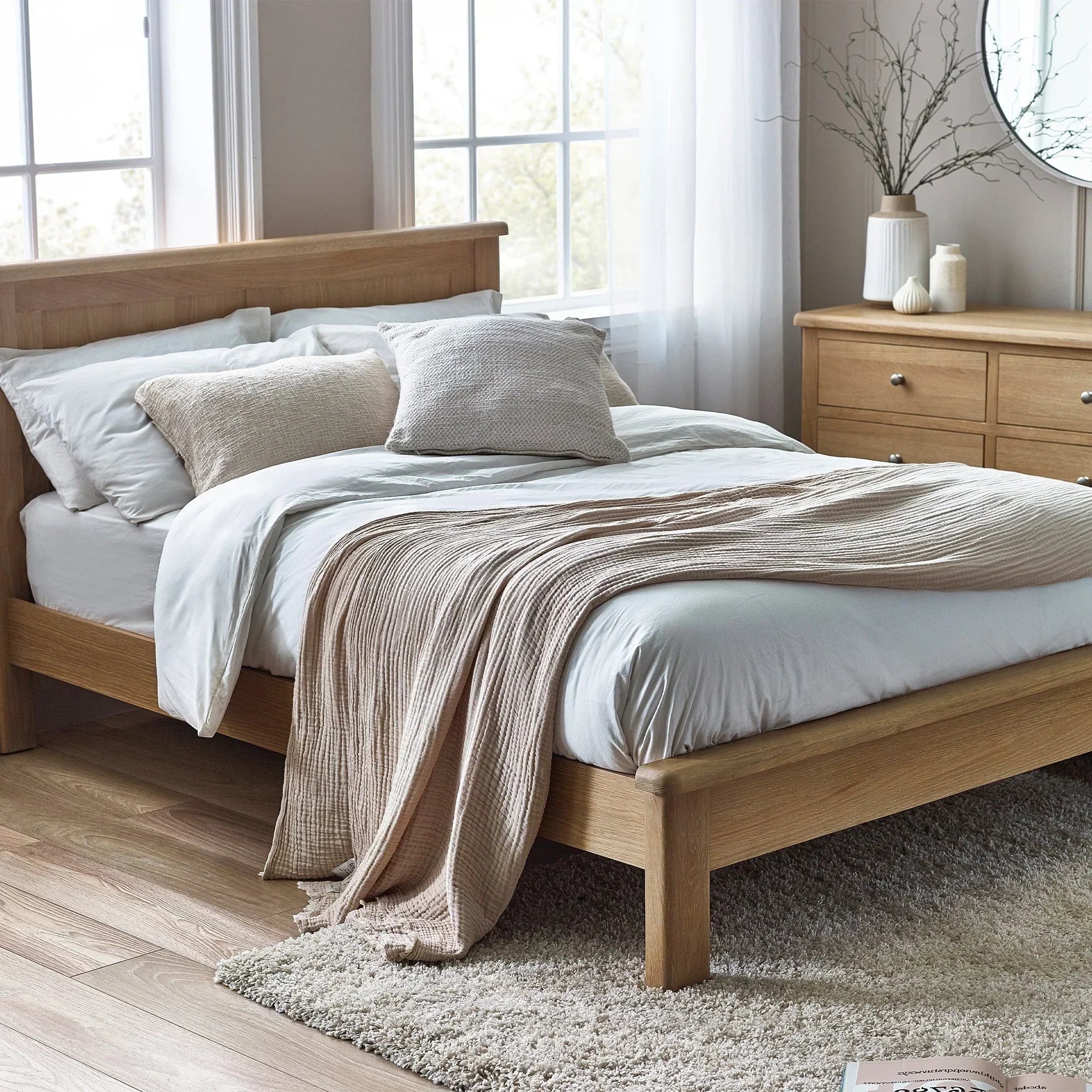 Limed oak bed frame with neutral bedding in bright bedroom, matching dresser and large window