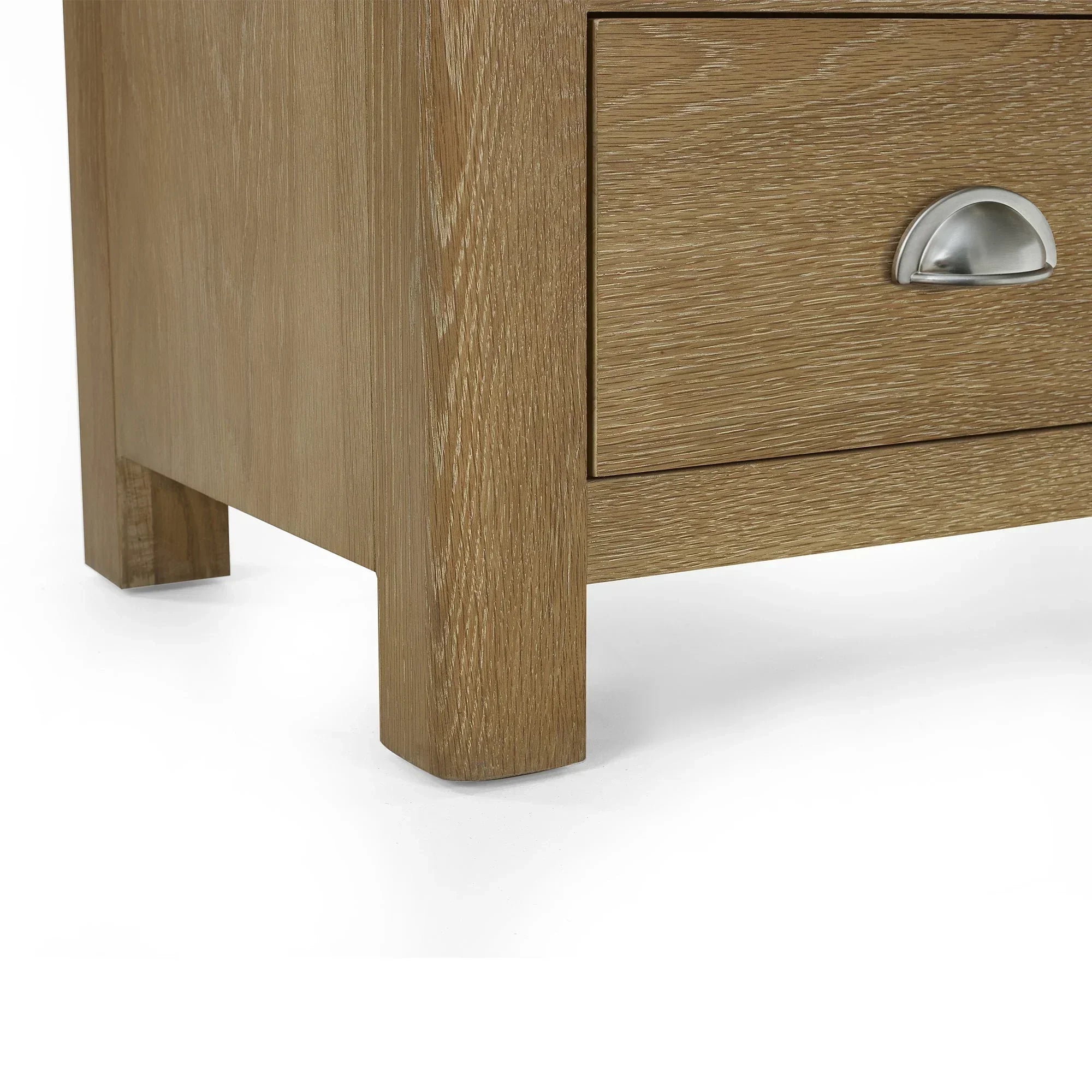 Closeup of limed oak chest of drawers leg and silver cup handle on bottom drawer