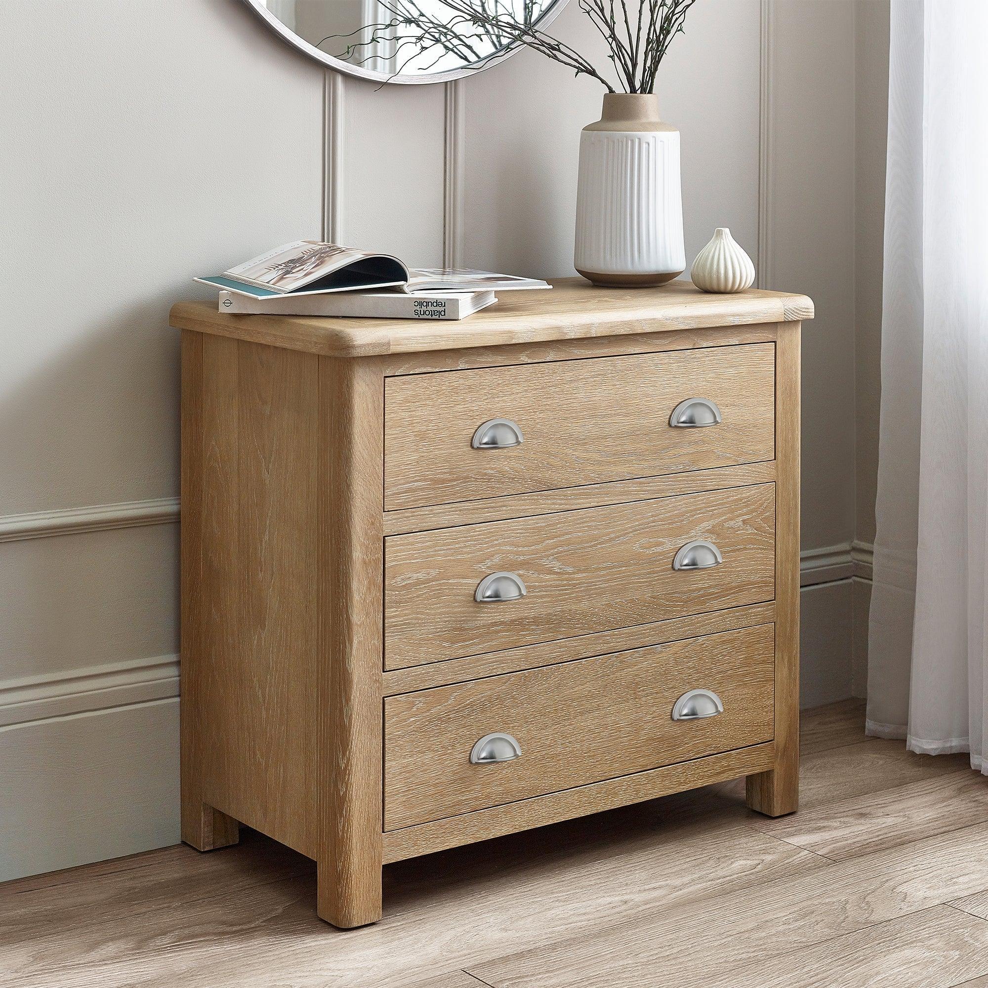 Limed oak 3 drawer chest with silver handles in a bright bedroom corner