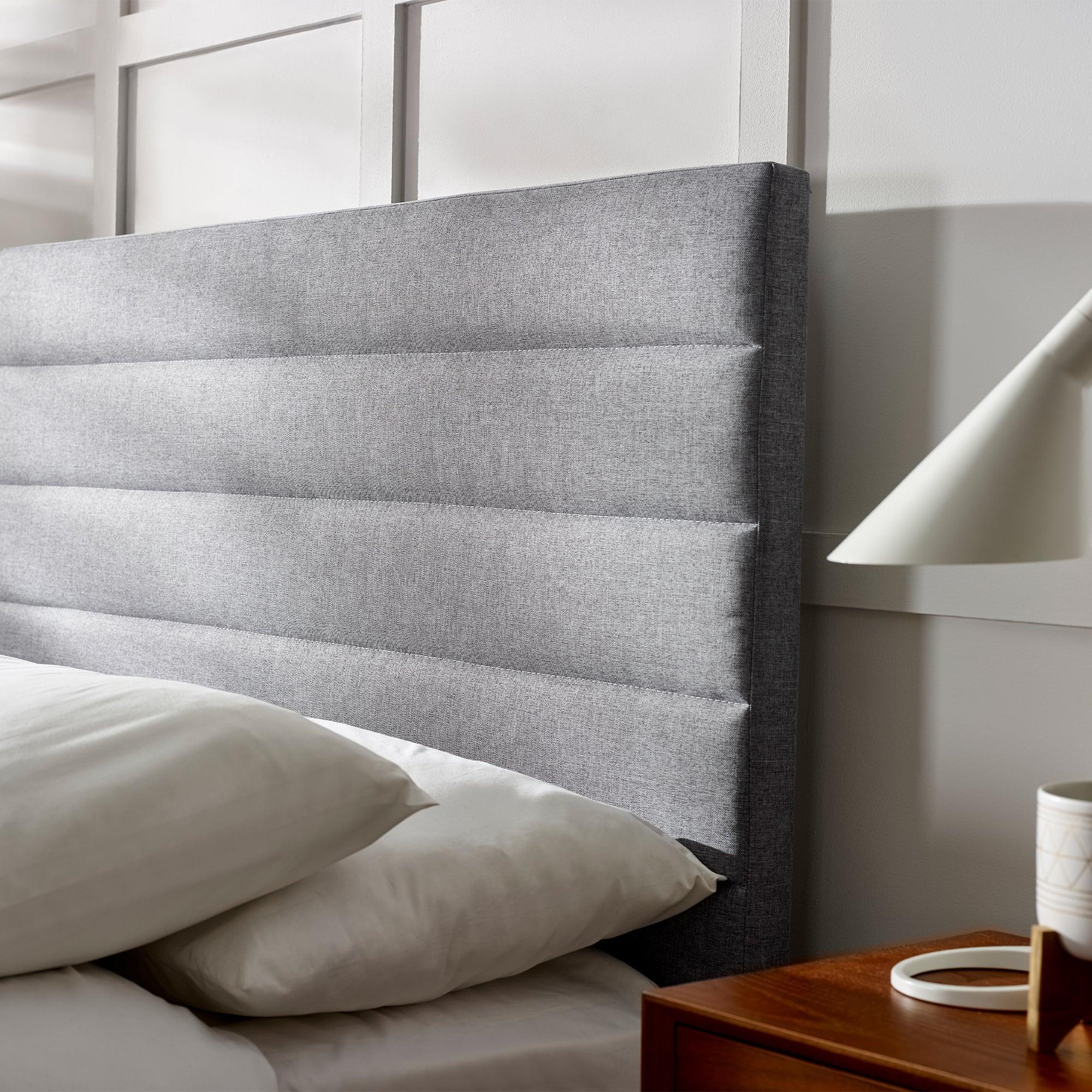 Grey upholstered bed headboard with horizontal panels beside wooden bedside table