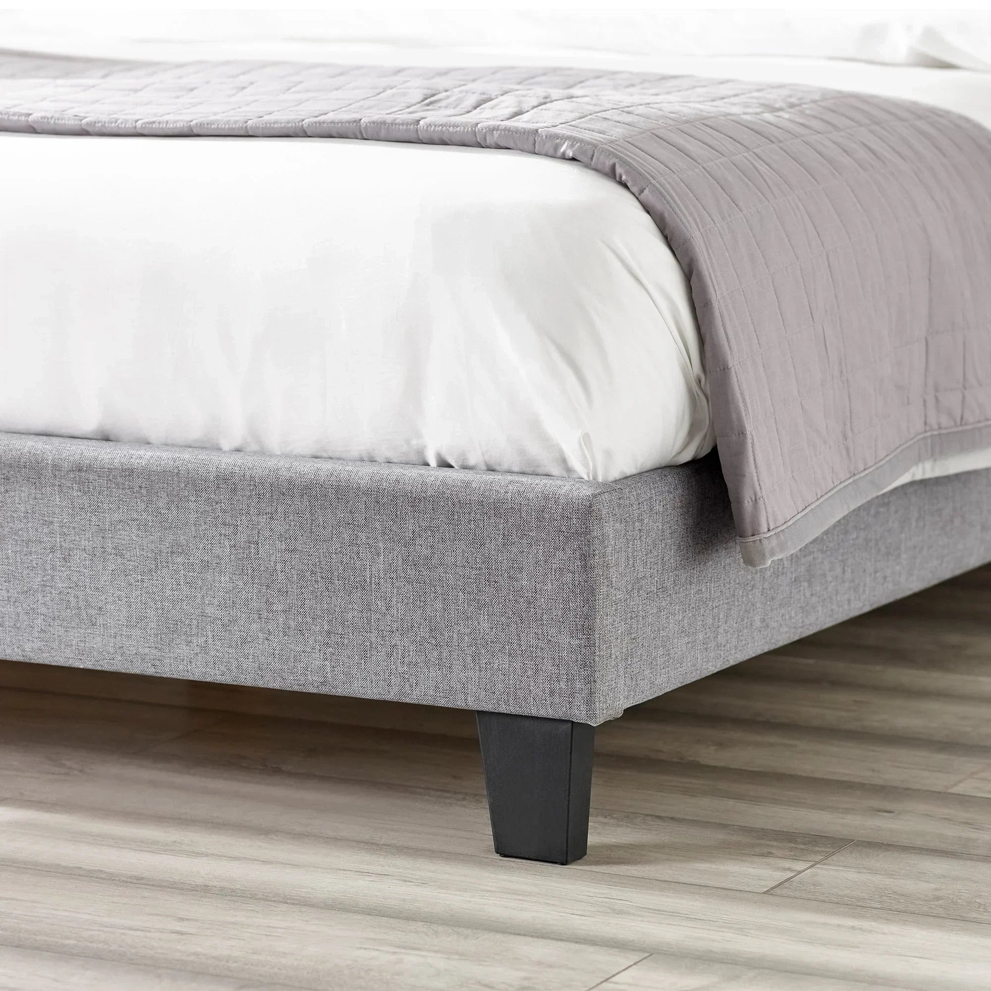 Light grey upholstered storage bed base with black legs and wooden flooring