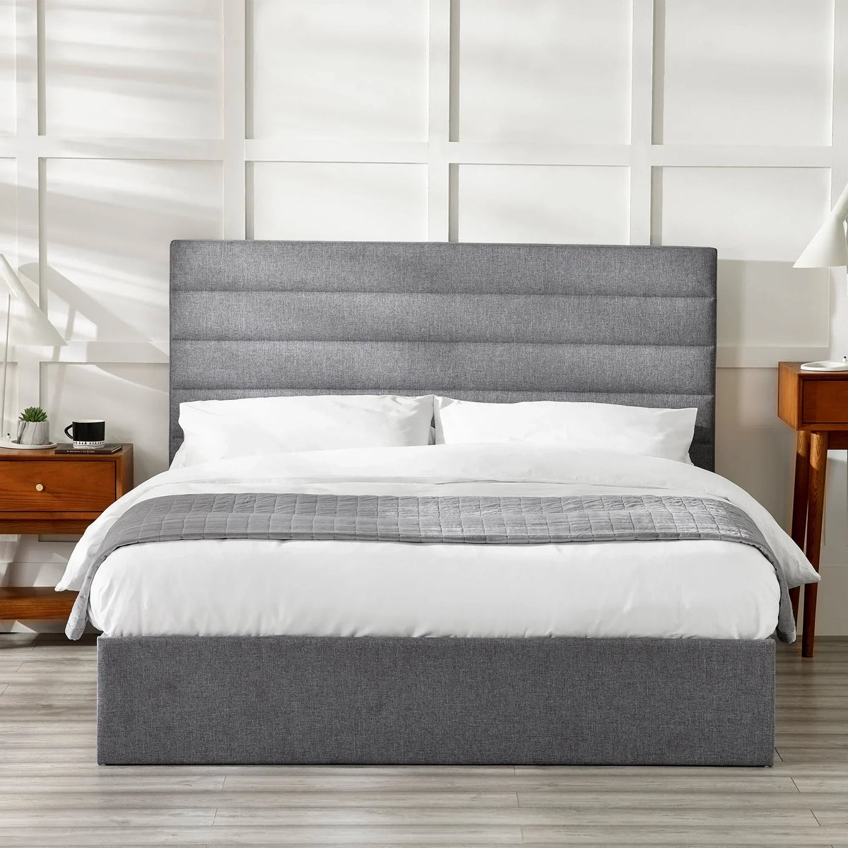 Grey upholstered storage bed with tall headboard, white bedding, wooden bedside tables