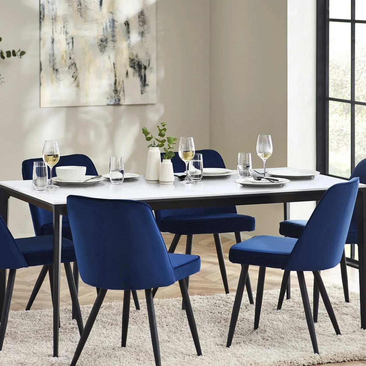 Rectangular stone top dining table with blue chairs and tableware in a bright dining room