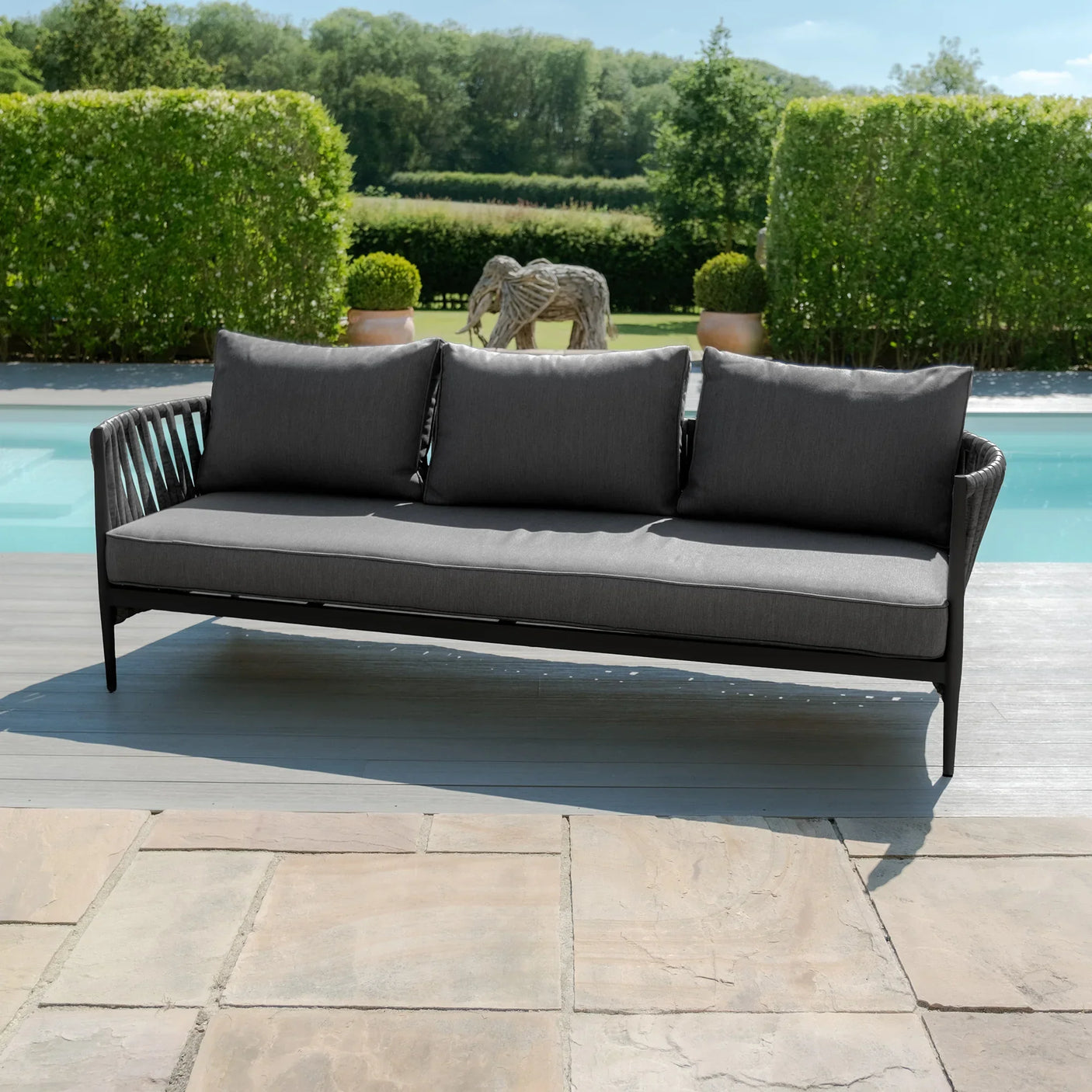 Charcoal grey outdoor sofa with rope armrests by a pool on a stone patio