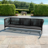 Black rope outdoor sofa on patio beside pool with greenery in background