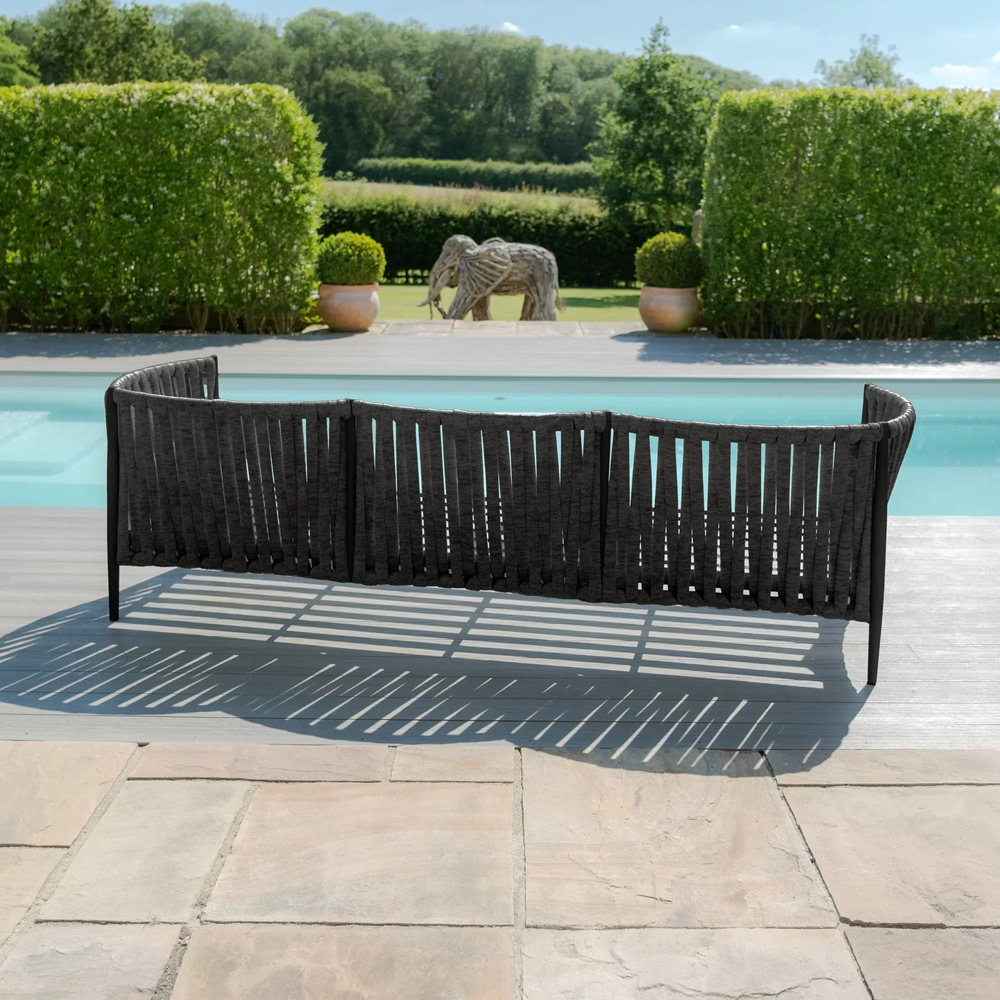 Charcoal outdoor sofa with woven rope back by a pool on a stone patio