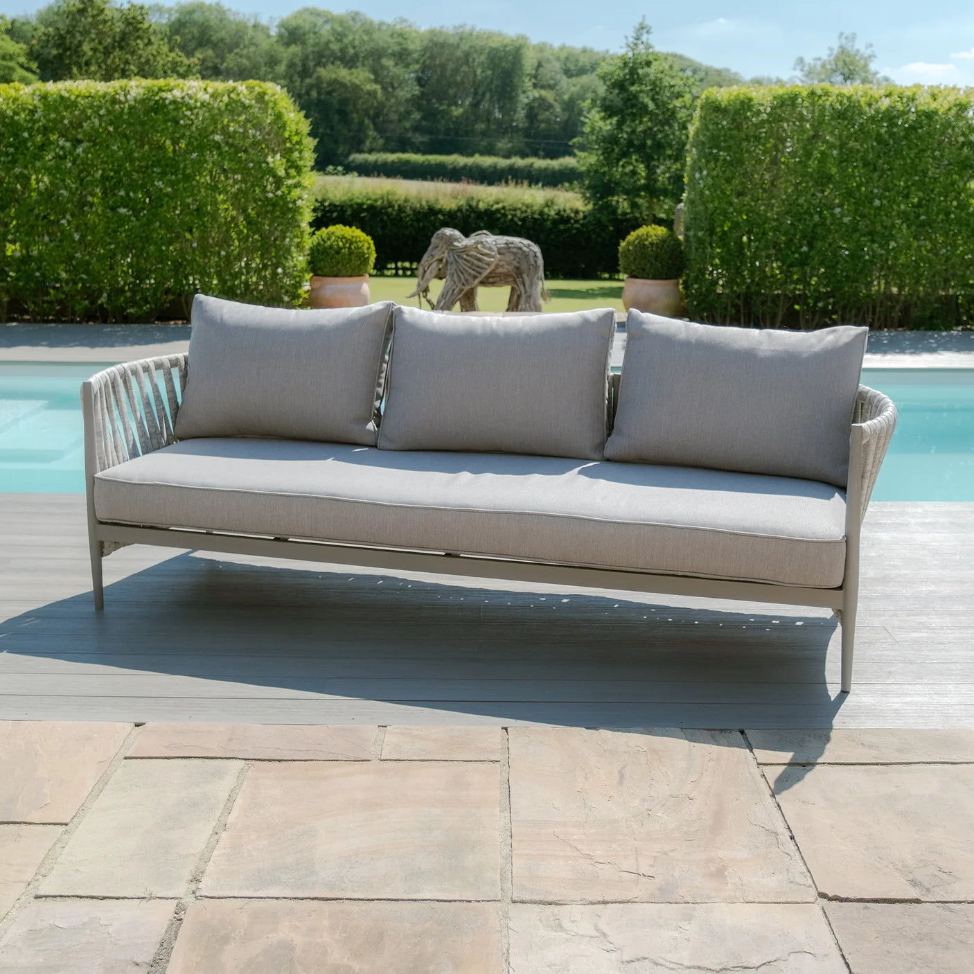 Outdoor rattan garden sofa with light grey cushions by swimming pool on patio