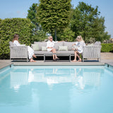 Grey outdoor sofa set with cushions and coffee table by pool, three women seated, summer day