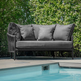 Grey outdoor sofa with cushions on patio beside swimming pool, surrounded by green hedges