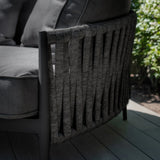 Close view of outdoor sofa with woven rope arm and dark grey cushions on decking