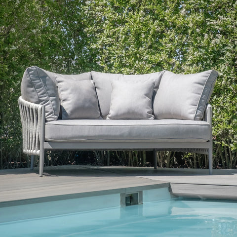 Light grey outdoor sofa with cushions on decking by pool and green hedges