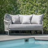 Light grey outdoor sofa with cushions on decking by pool and green hedges