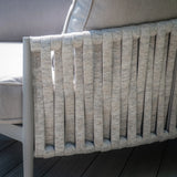 Close-up of woven rope sofa arm detail with light grey cushion on wooden deck