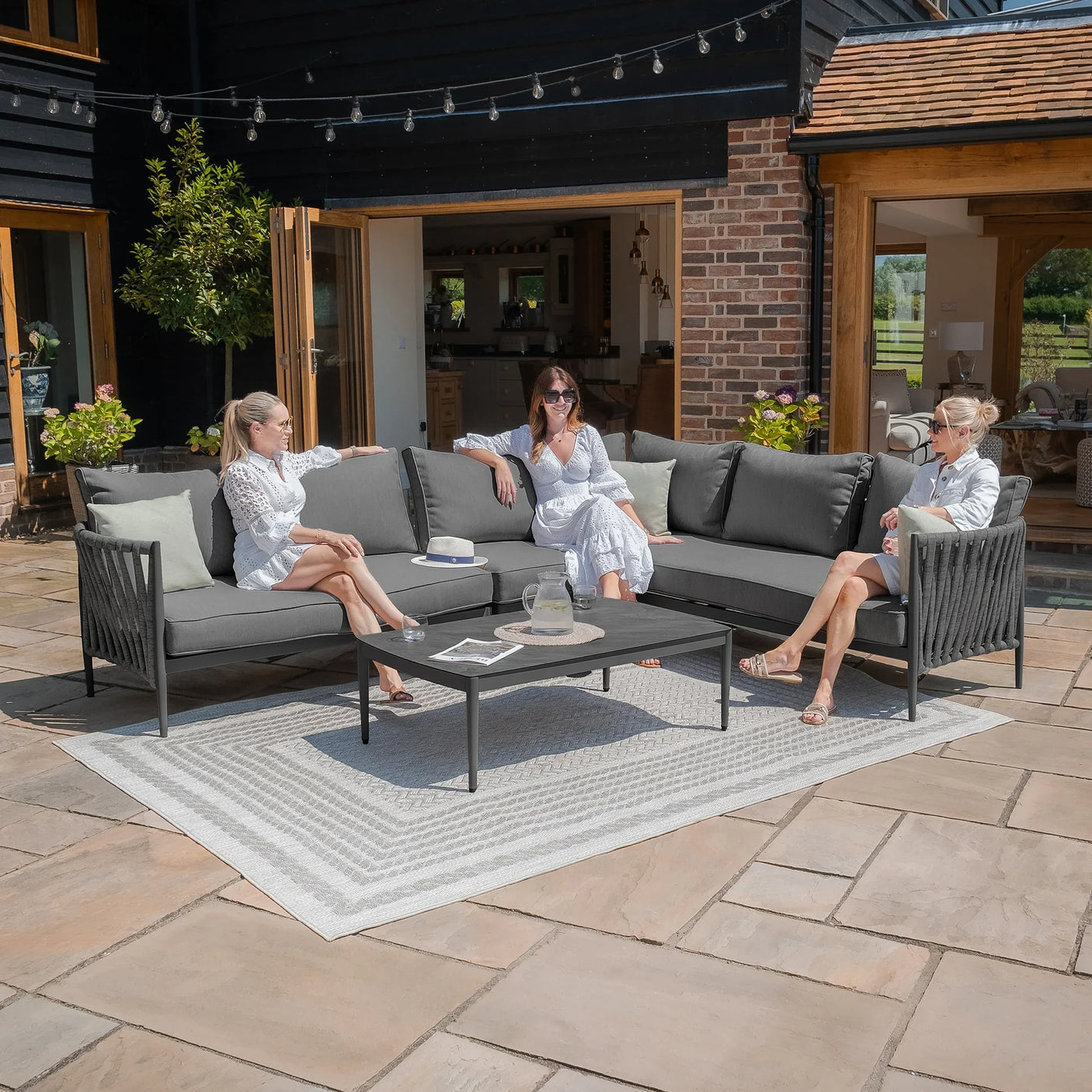 Grey outdoor corner sofa set with black metal frame and coffee table on patio tiles