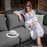 Grey outdoor sofa set with woman in white dress and straw hat on cushion in patio setting