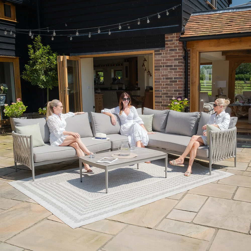 Grey outdoor corner sofa set with cushions and coffee table on a stone patio