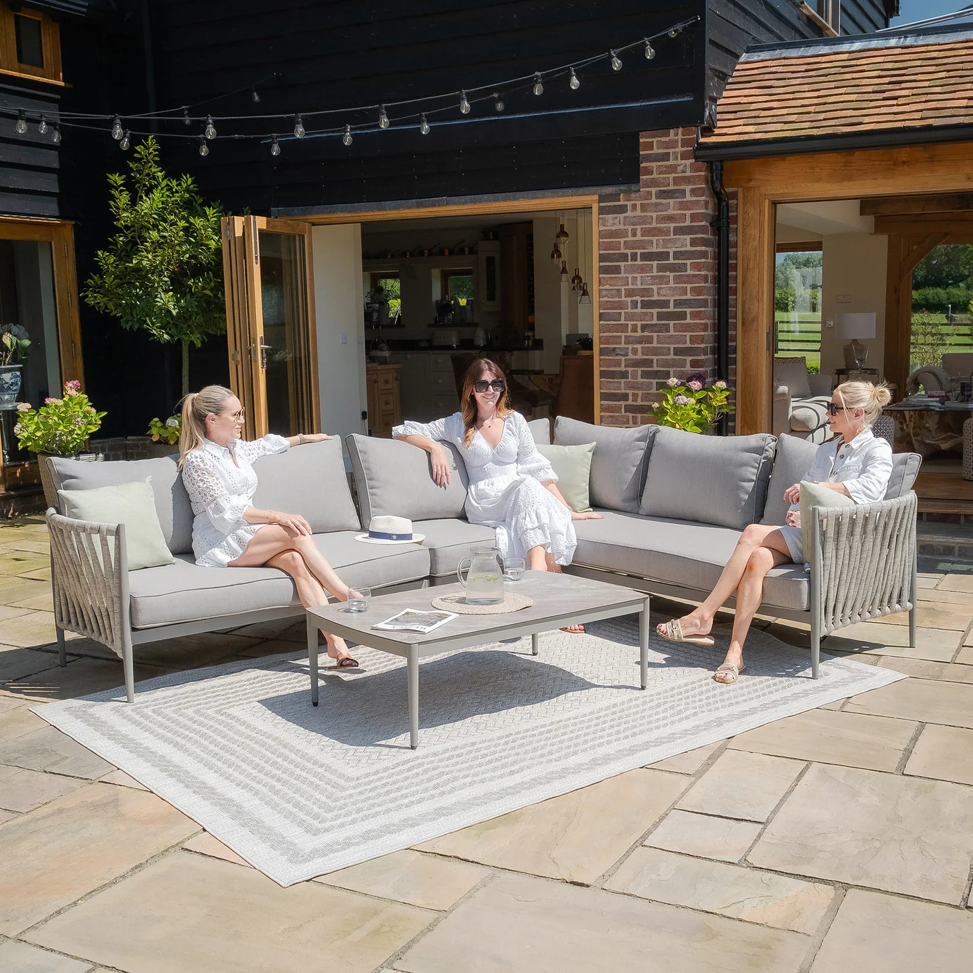 Grey outdoor corner sofa set with cushions and coffee table on a stone patio