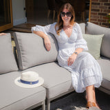 Light grey outdoor sofa with cushions on patio, woman sitting, sunhat placed beside her