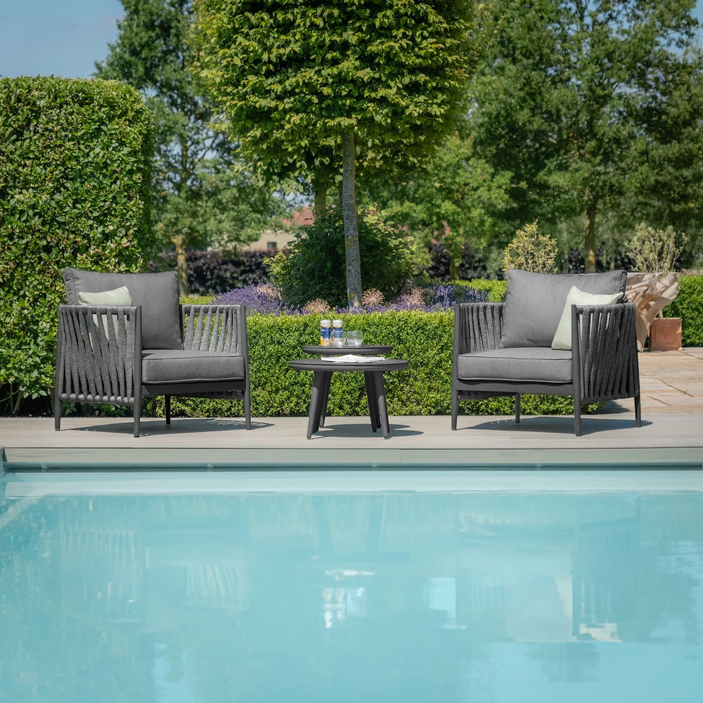 Outdoor rope armchairs and round table set beside pool on garden patio