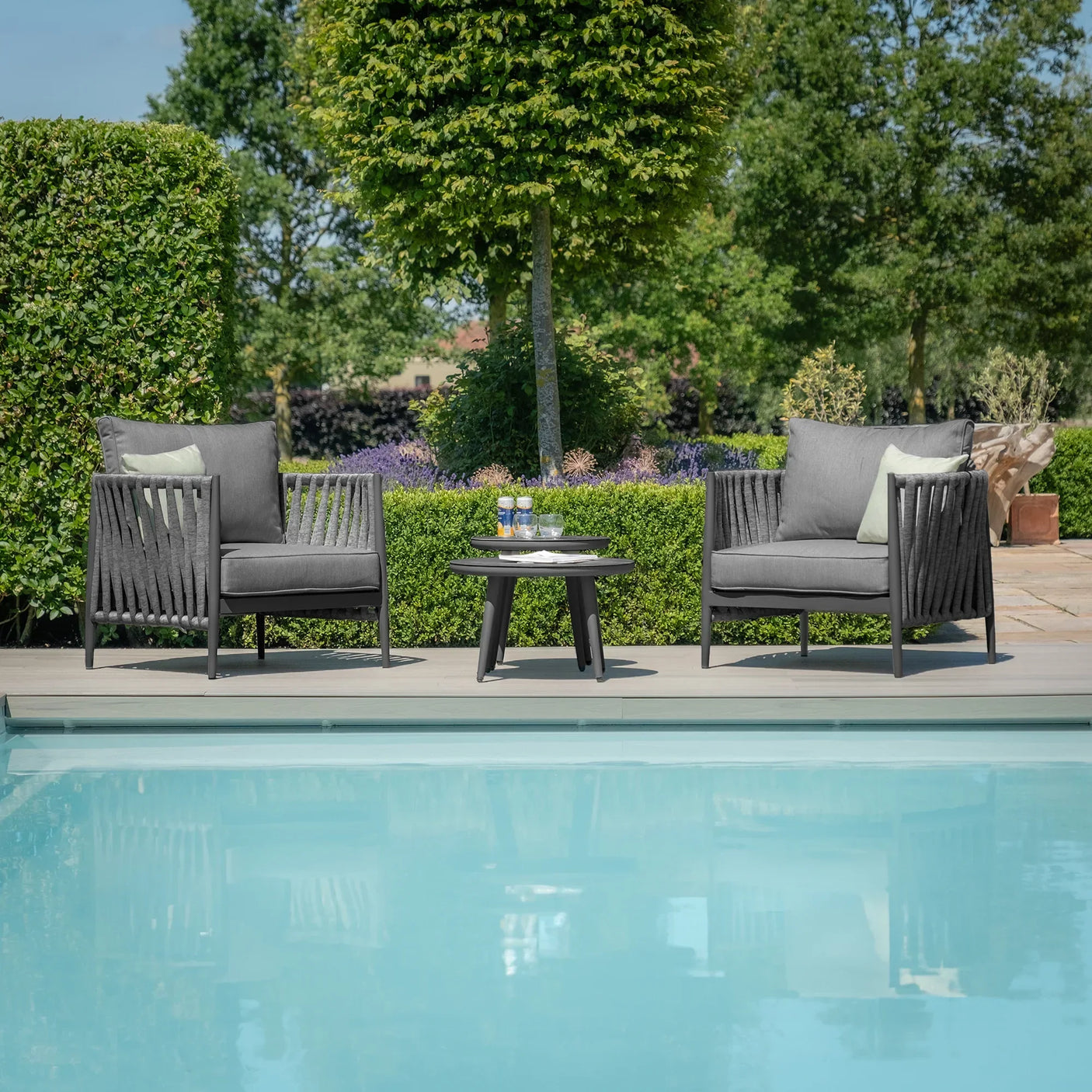 Outdoor rope armchairs and round table set beside pool on garden patio