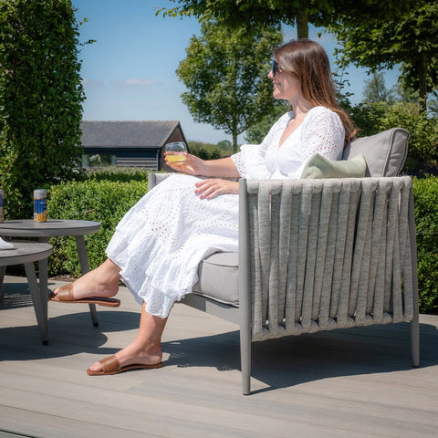 Outdoor lounge chair with grey cushions and rope detailing on patio, side table nearby