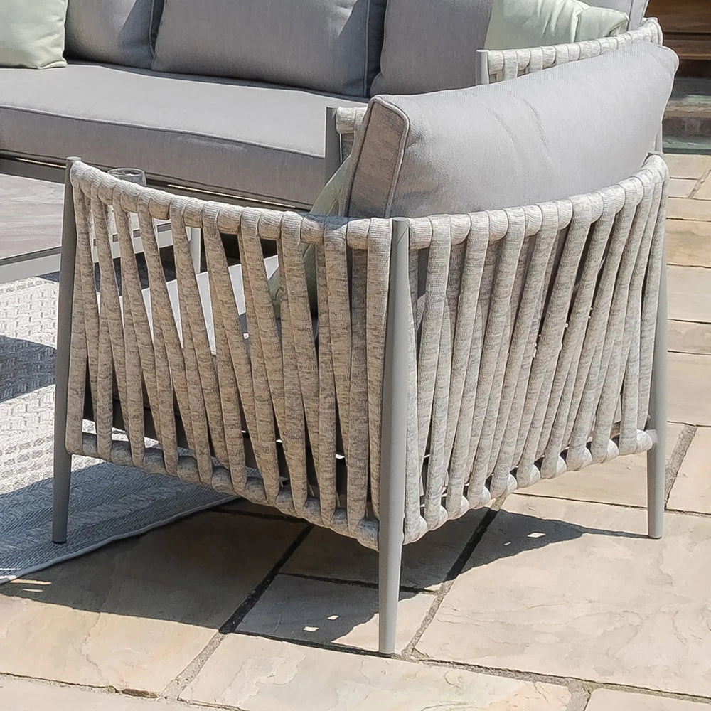 Light grey outdoor lounge chair with woven rope sides and cushion on stone patio