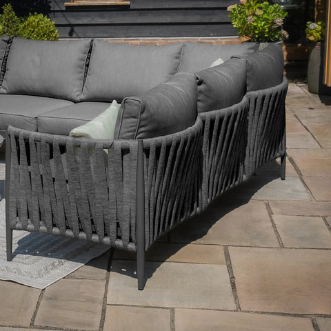 Grey outdoor sofa set with rope backrest and cushions on a stone patio
