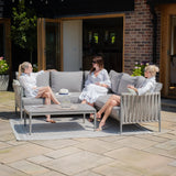Grey outdoor sofa set with cushions and coffee table on patio, three women seated in garden