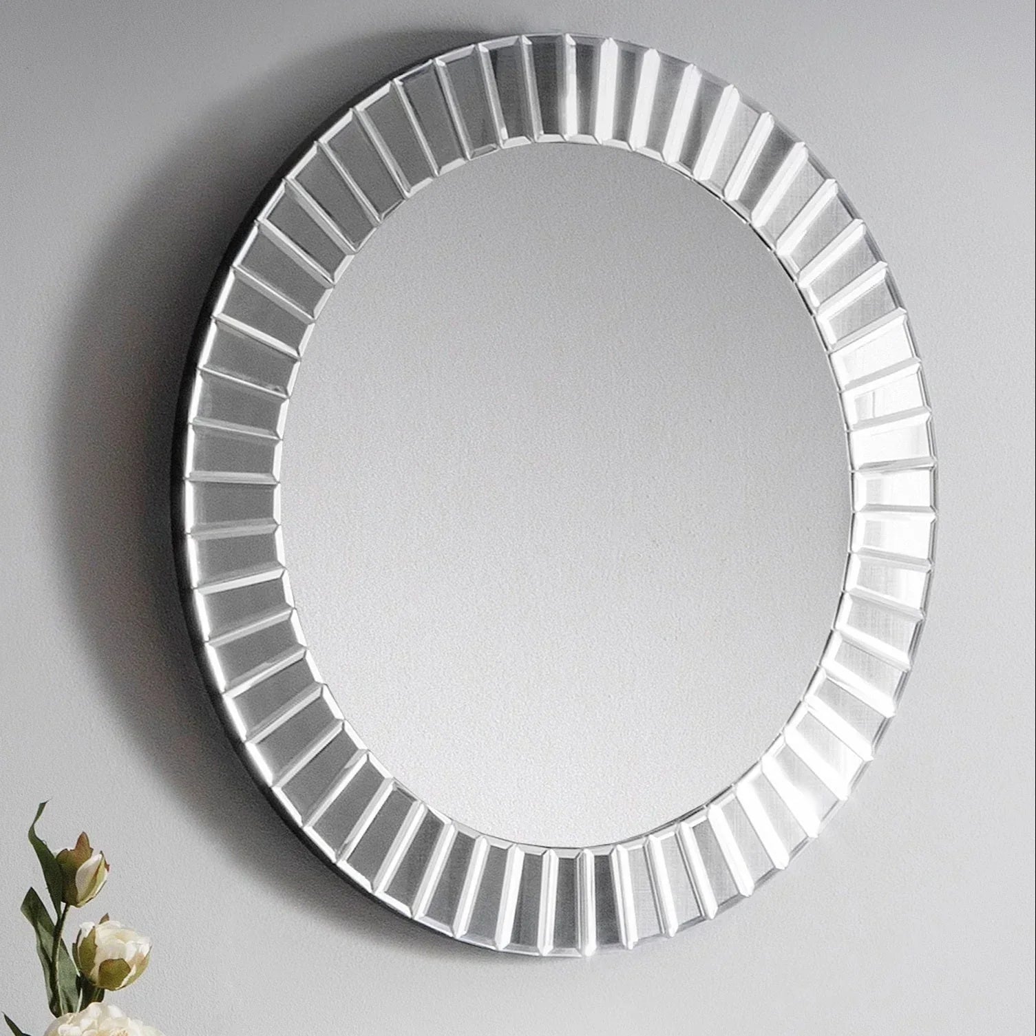 Round mirror with beveled frame on grey wall, decorative flowers visible at lower left corner