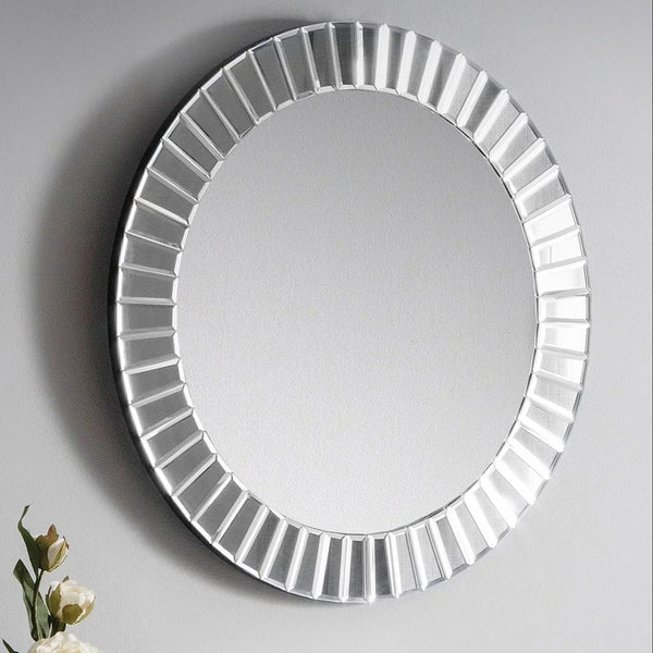 Round mirror with beveled frame on grey wall, decorative flowers visible at lower left corner