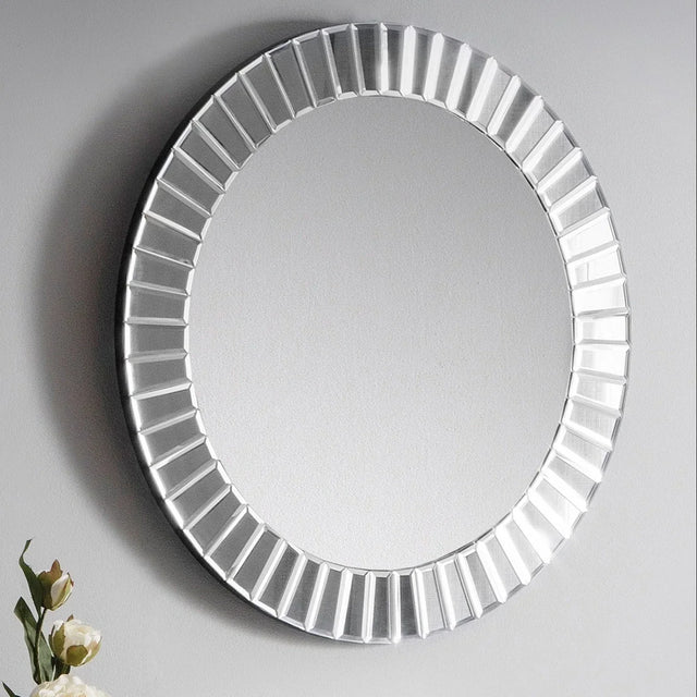 Round mirror with beveled frame on grey wall, decorative flowers visible at lower left corner