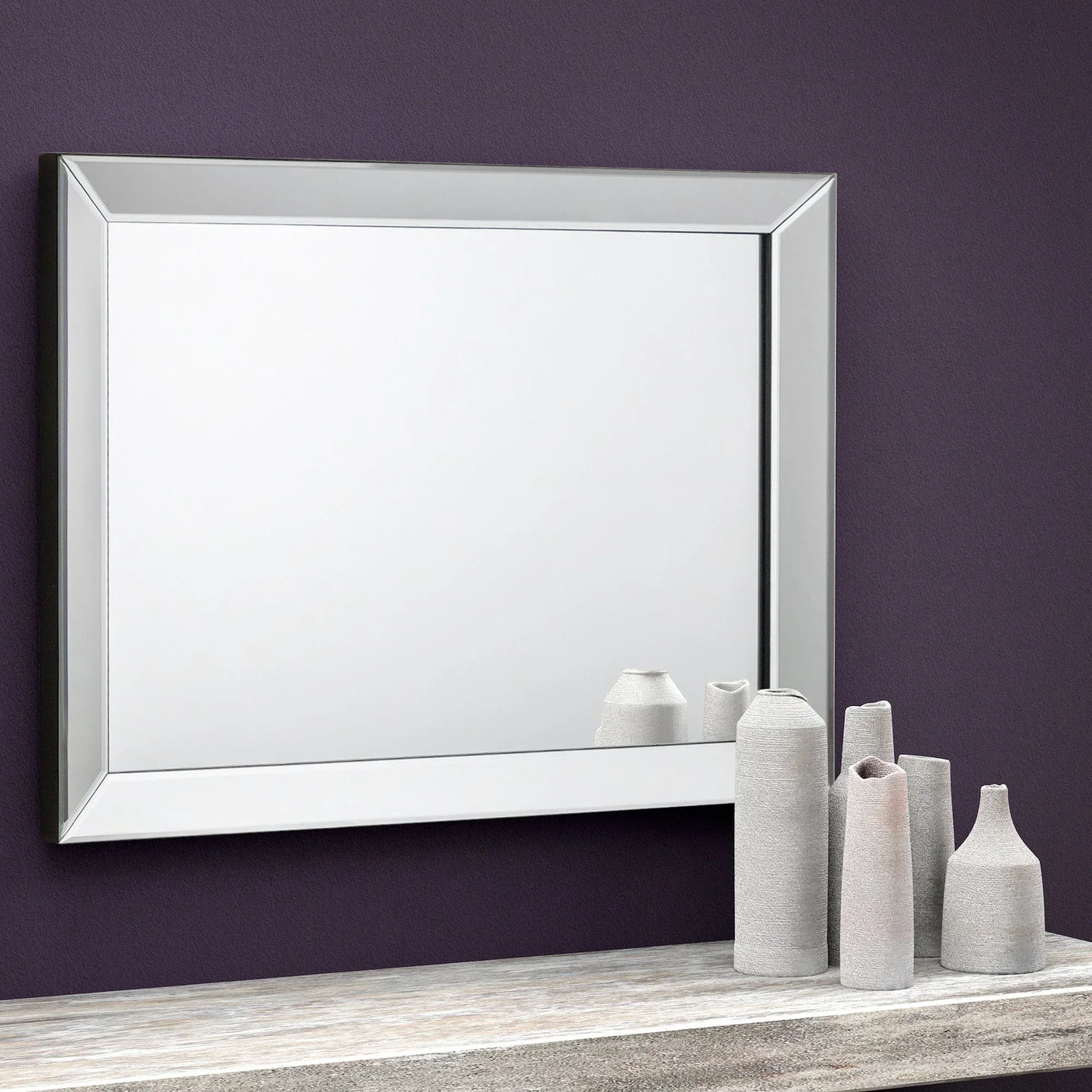 Soprano wall mirror with beveled edge above console table and ceramic vases on purple wall