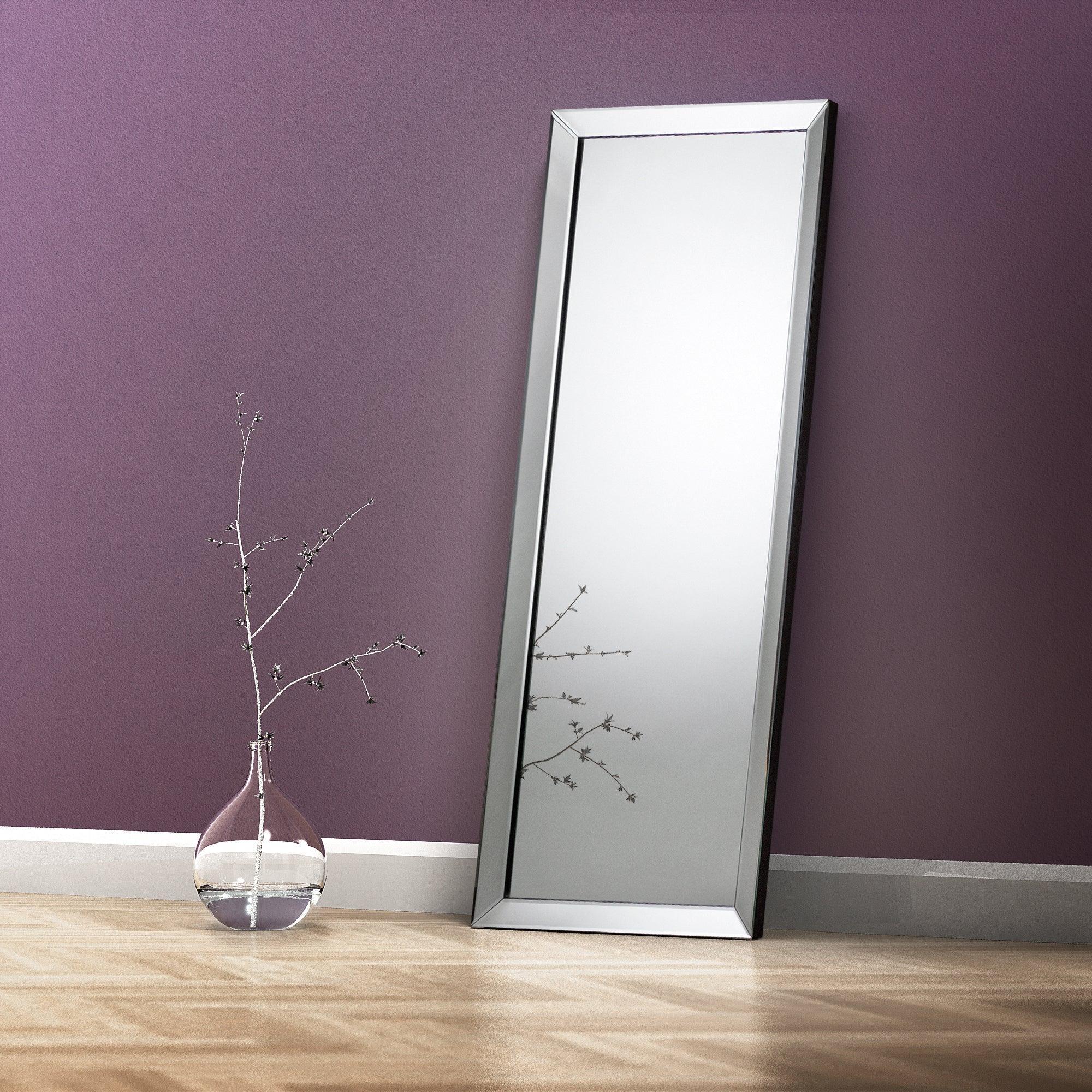 Rectangular dress mirror with silver frame leaning against purple wall on wood floor