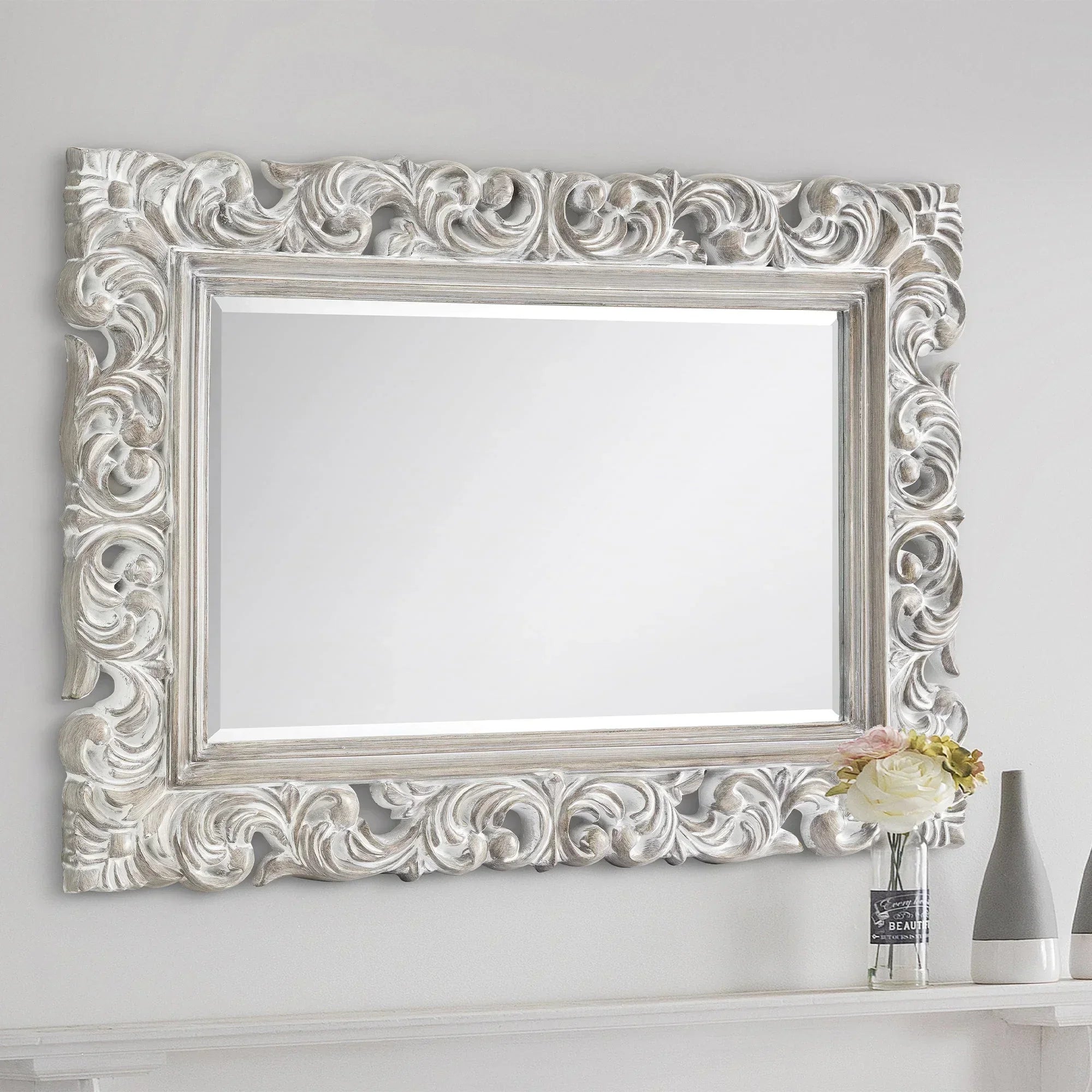 Baroque distressed wall mirror with ornate silver frame above shelf and floral decor