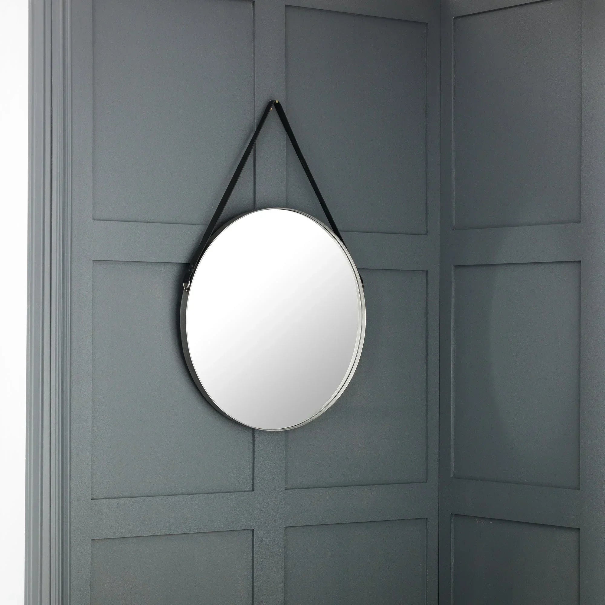 Round wall mirror with black strap hanging on grey panelled wall