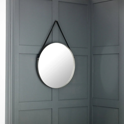 Round wall mirror with black strap hanging on grey panelled wall