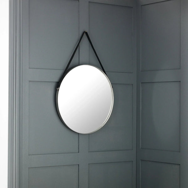 Round wall mirror with black strap hanging on grey panelled wall