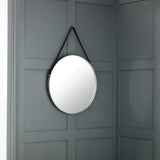 Round wall mirror with black strap hanging on grey panelled wall
