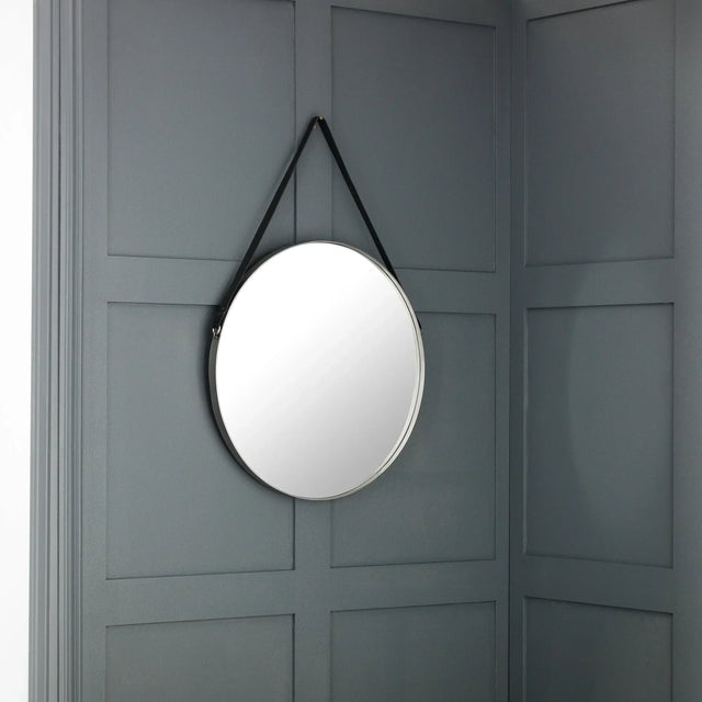 Round wall mirror with black strap hanging on grey panelled wall