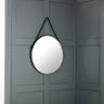 Round wall mirror with black strap hanging on grey panelled wall