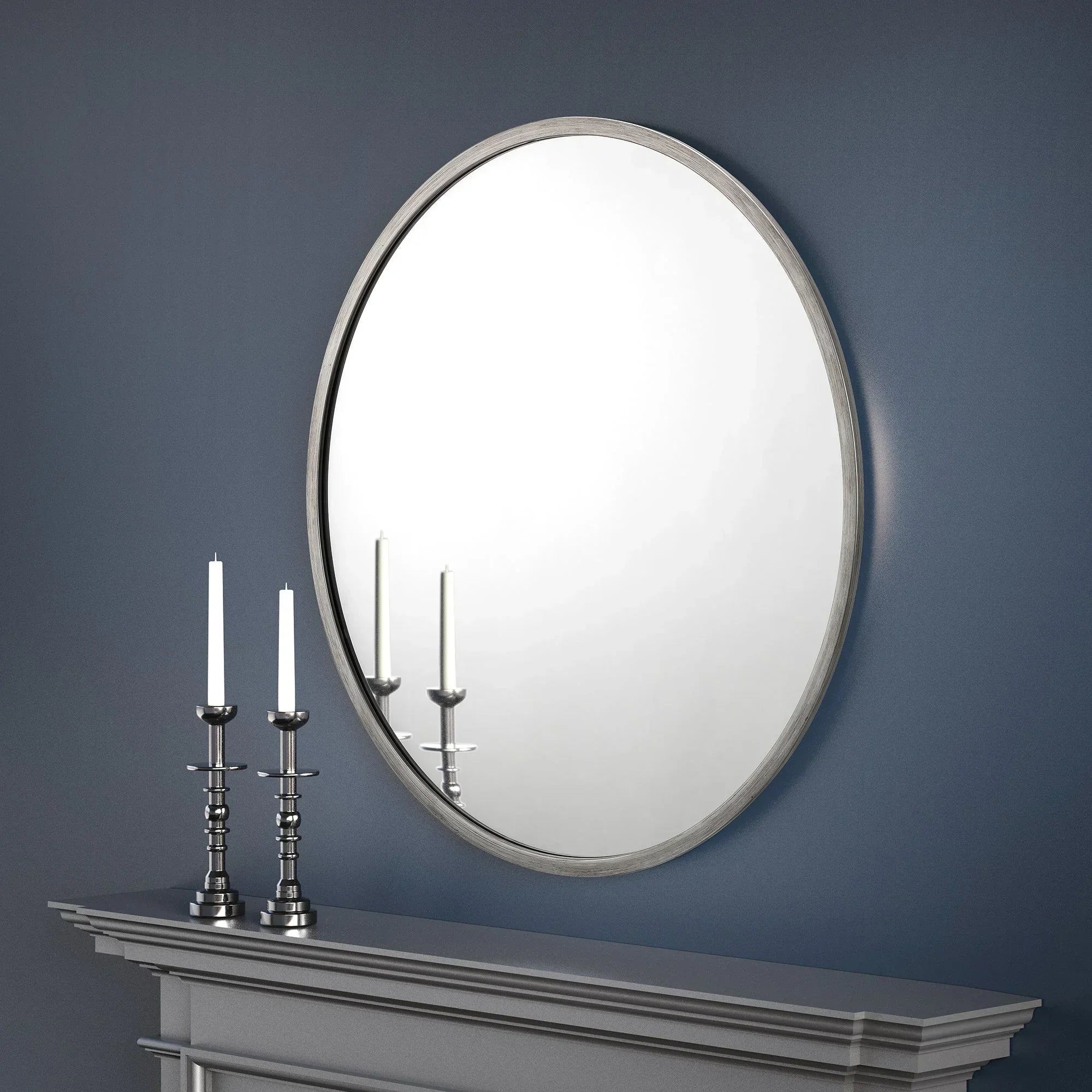 Round pewter mirror above grey mantel with two silver candlesticks against blue wall