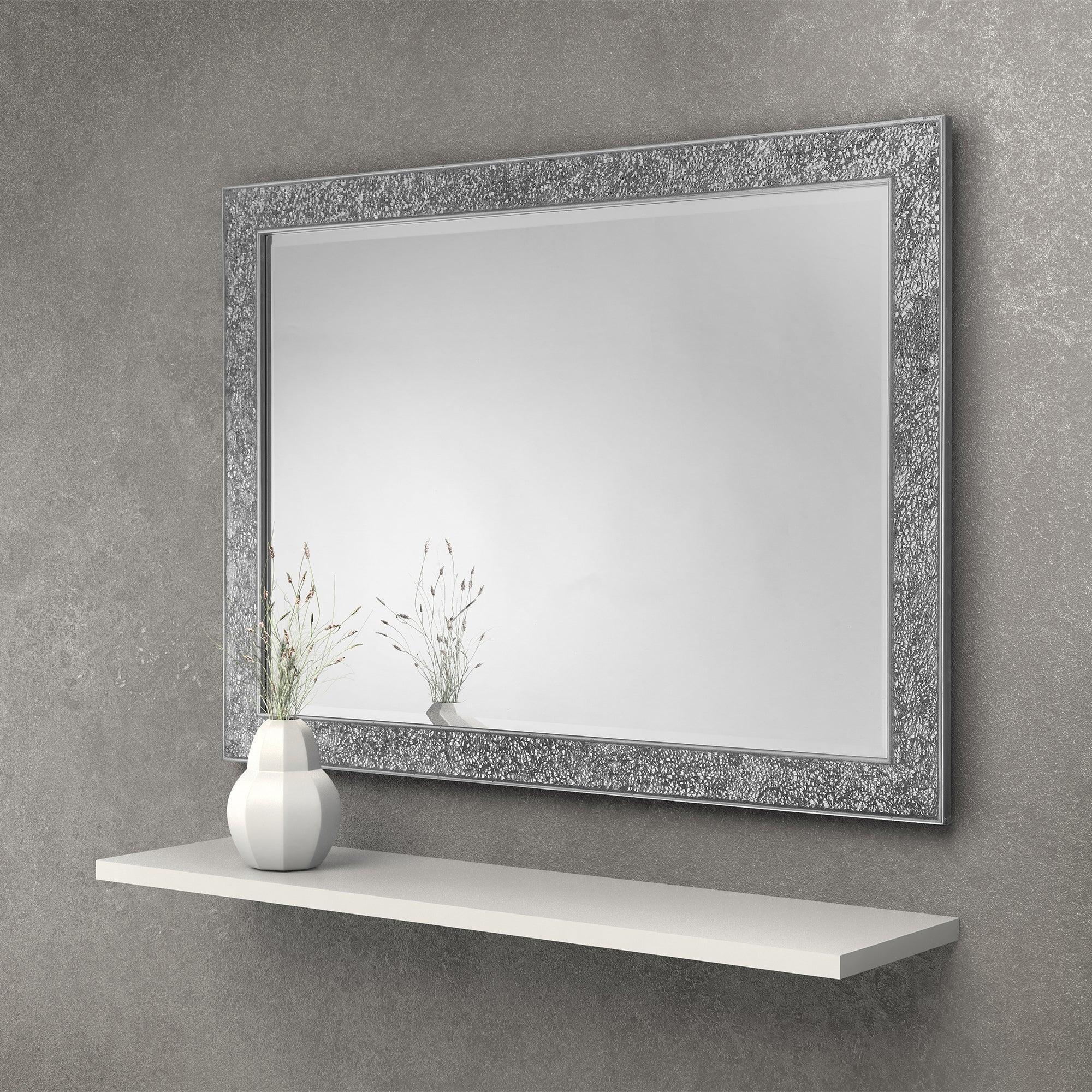 Rectangular wall mirror with decorative silver textured frame above a white floating shelf